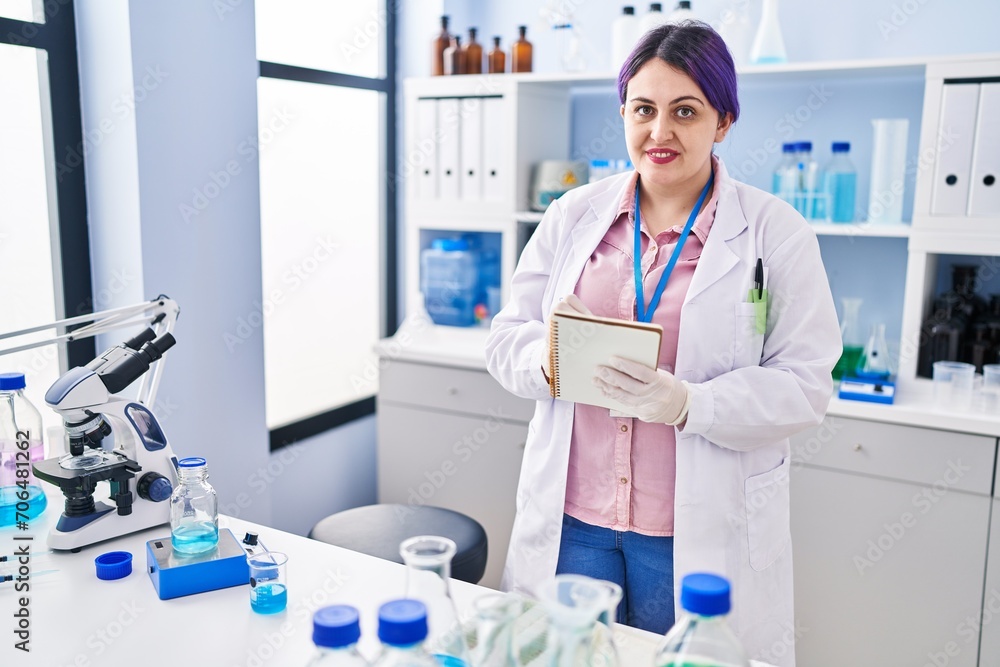 Young beautiful plus size woman scientist writing on notebook at laboratory