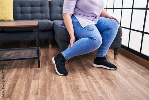 Young beautiful plus size woman sitting on sofa suffering for leg paing at home