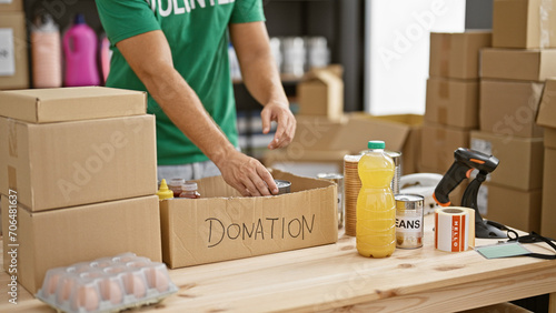 A young man prepares a donation box with food items in a warehouse setting, reflecting charity and community service. © Krakenimages.com
