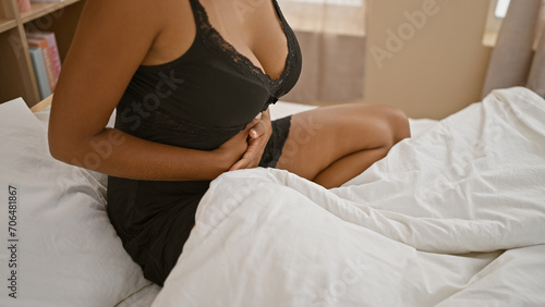 African american woman with stomach pain sitting in bed