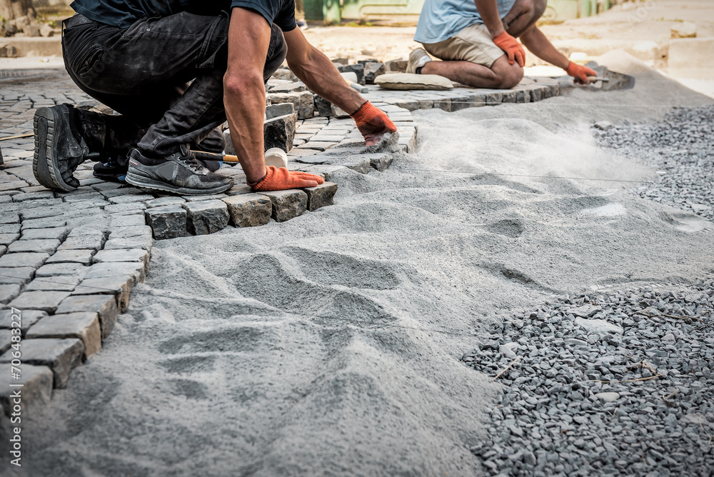 Construction workers installing and laying pavement stones on street, road or sidewalk. Worker using stones and rubber hammer to build stone sidewalk Construction workers installing and laying pavement stones on street, road or sidewalk. Worker using stones and rubber hammer to build stone sidewalk
