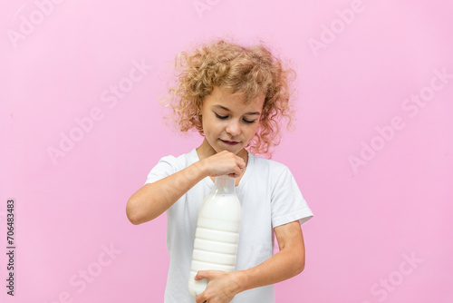 Little girl with a bottle of milk on a pink background