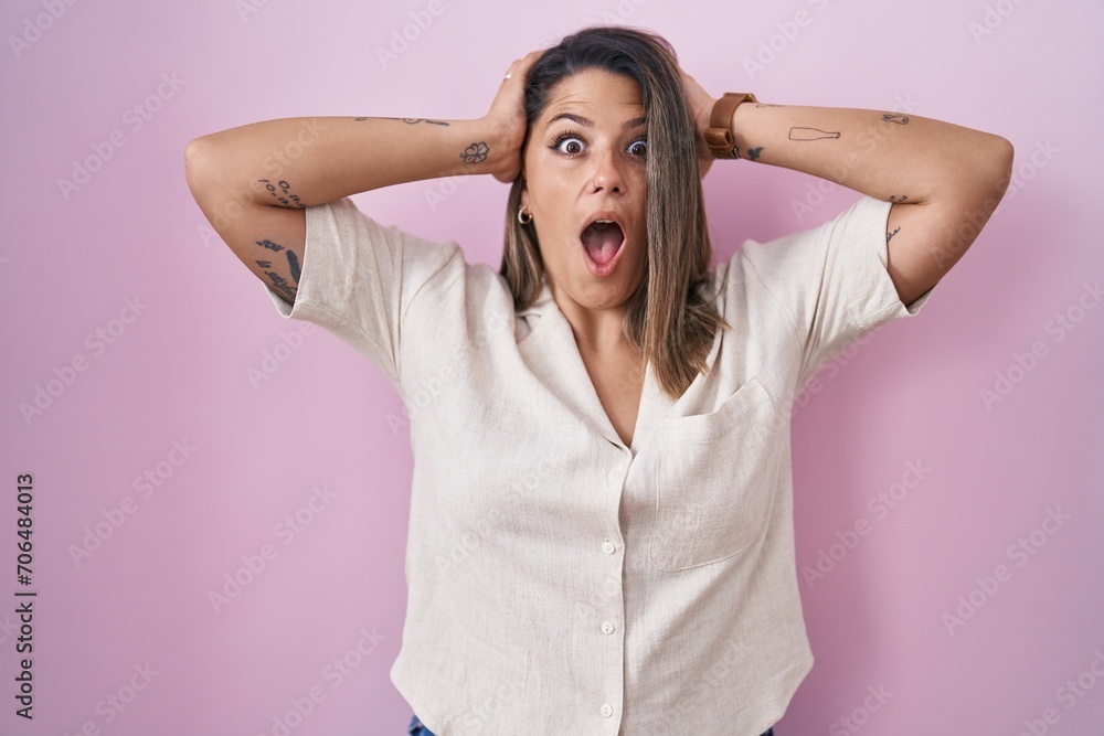 Blonde woman standing over pink background crazy and scared with hands on head, afraid and surprised of shock with open mouth Blonde woman standing over pink background crazy and scared with hands on head, afraid and surprised of shock with open mouth