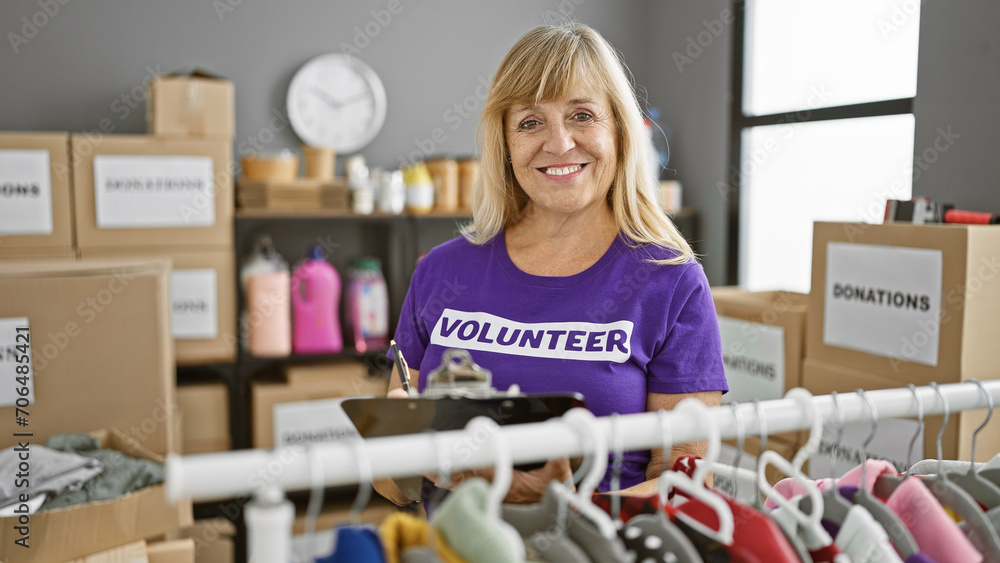 Heartwarming sight of smiling, beautiful, blonde middle age woman, energetically checking and taking notes on donated clothes at lively charity center Heartwarming sight of smiling, beautiful, blonde middle age woman, energetically checking and taking notes on donated clothes at lively charity center