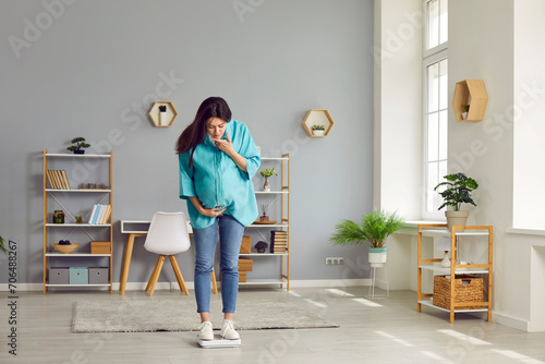 Expectant mother weighs herself on scales at home. Young pregnant woman stands on scales in the living room and looks down at figures to see how much she has gained. Pregnancy, health, weight concept