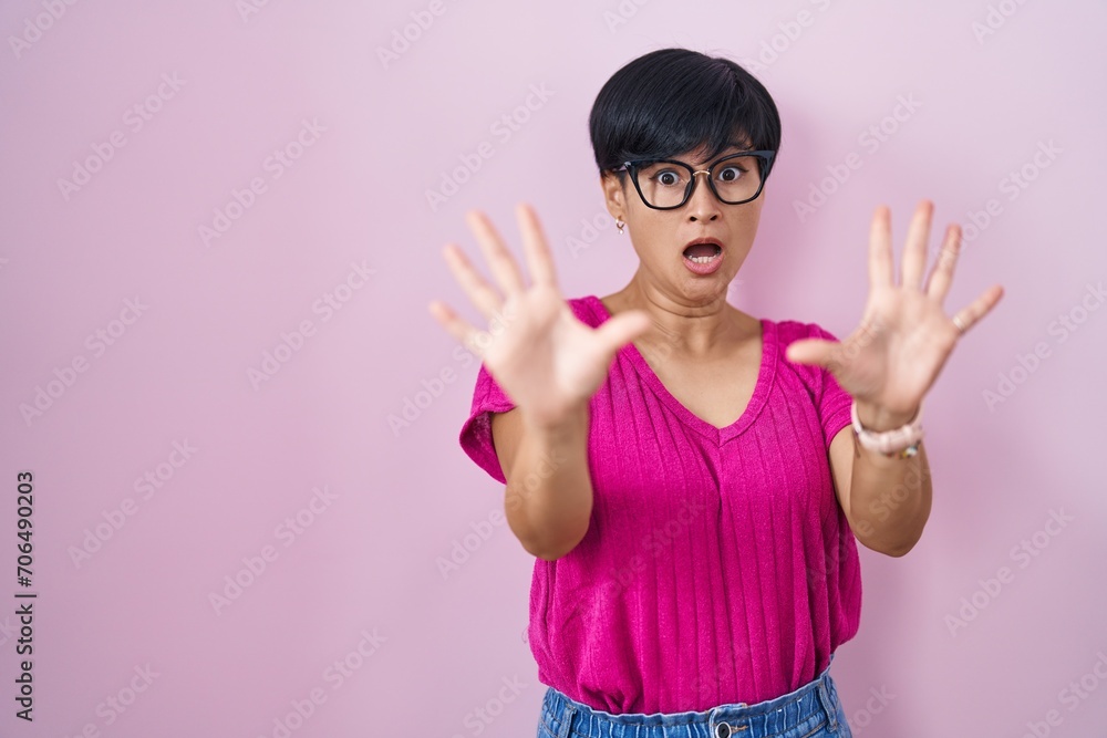Young asian woman with short hair standing over pink background afraid and terrified with fear expression stop gesture with hands, shouting in shock. panic concept. Young asian woman with short hair standing over pink background afraid and terrified with fear expression stop gesture with hands, shouting in shock. panic concept.
