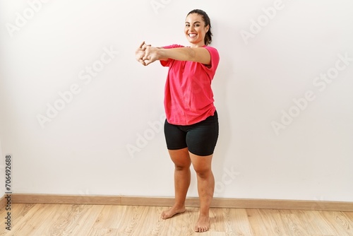 Young beautiful hispanic woman smiling confident stretching arms at sport center