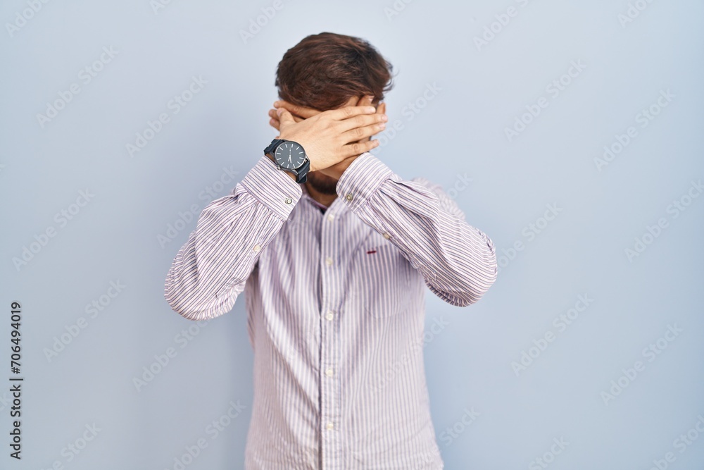 Arab man with beard standing over blue background covering eyes and mouth with hands, surprised and shocked. hiding emotion Arab man with beard standing over blue background covering eyes and mouth with hands, surprised and shocked. hiding emotion