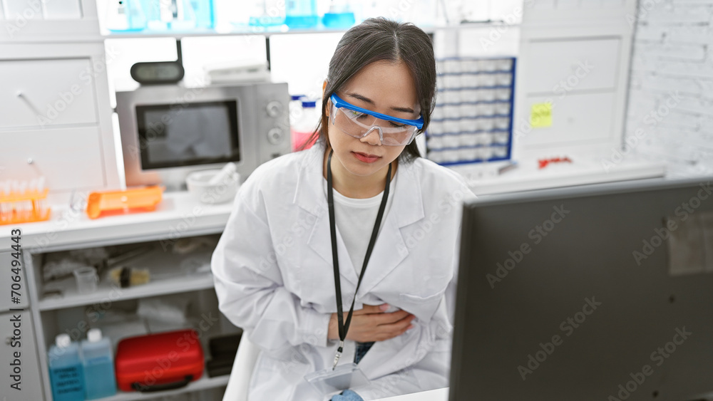 A young asian woman scientist wearing safety glasses feels stomachache in a laboratory setting