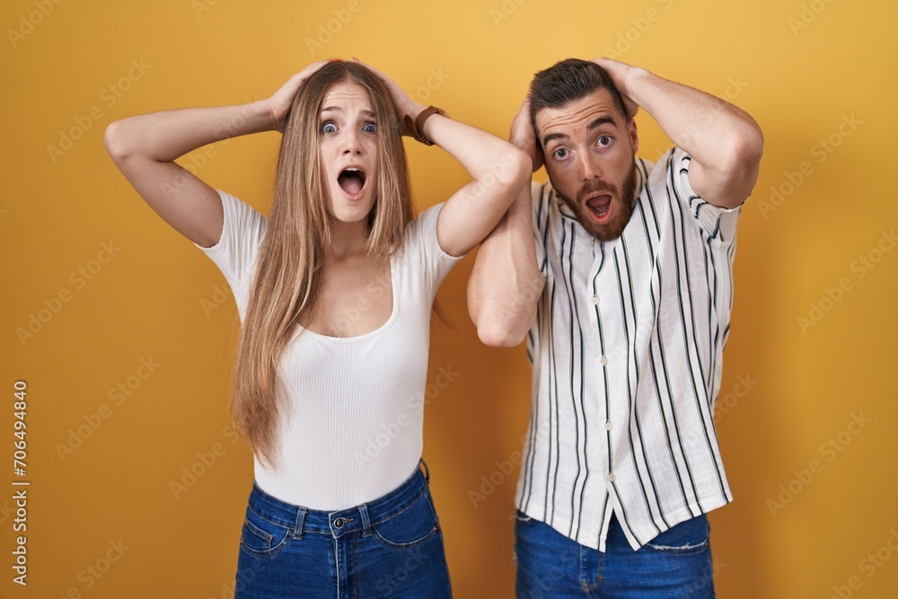 Young couple standing over yellow background crazy and scared with hands on head, afraid and surprised of shock with open mouth Young couple standing over yellow background crazy and scared with hands on head, afraid and surprised of shock with open mouth