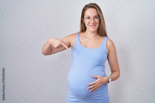 Young pregnant woman standing over white background looking confident with smile on face  pointing oneself with fingers proud and happy.