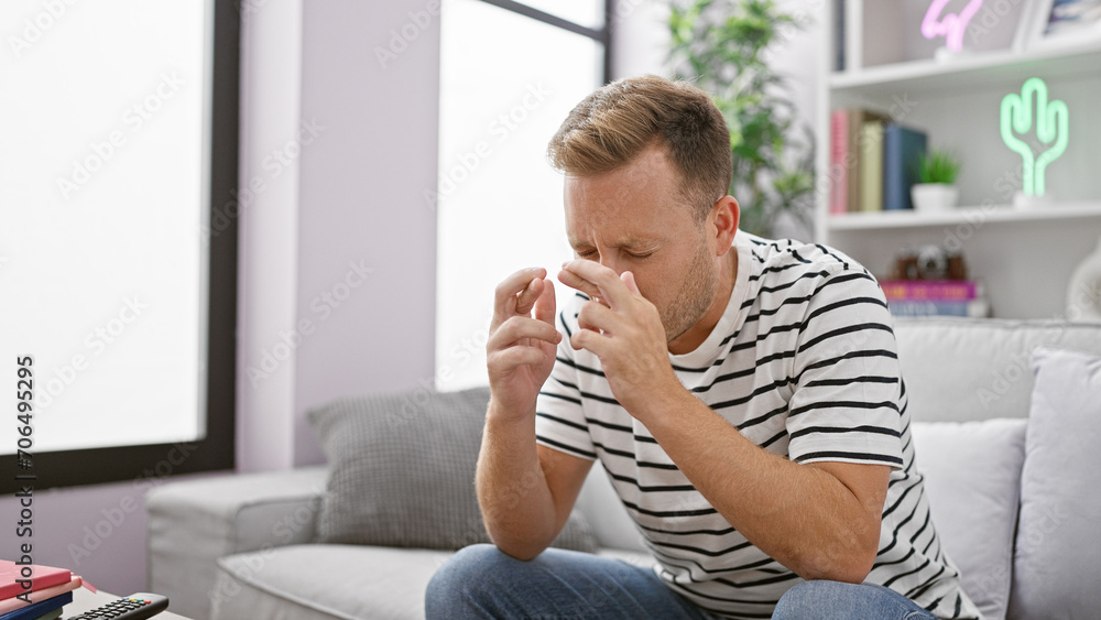 Hopeful young caucasian man at home, crossing fingers for a stroke of luck, sitting seriously relaxed on living room sofa, indoor background showing an expressive reality of the person. Hopeful young caucasian man at home, crossing fingers for a stroke of luck, sitting seriously relaxed on living room sofa, indoor background showing an expressive reality of the person.