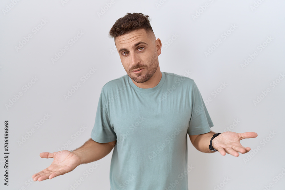 Hispanic man with beard standing over white background clueless and confused with open arms, no idea concept.