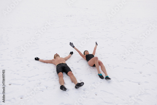 People laying in the snow wearing swimsuit. Young couple after winter sauna. Cold exposure for better health and mood. Swim in ice cold water.