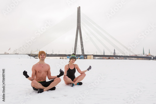 A youthful pair adopts a lotus pose post-winter sauna, embracing cold exposure for enhanced health and mood. They take a refreshing dip in icy water as part of their immune-boosting routine.