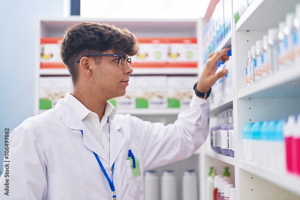 Young hispanic teenager pharmacist holding product on shelving at pharmacy