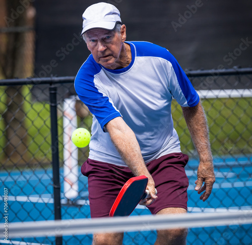 Senior man applies slice to the whiffle ball that is used in pickleball tif