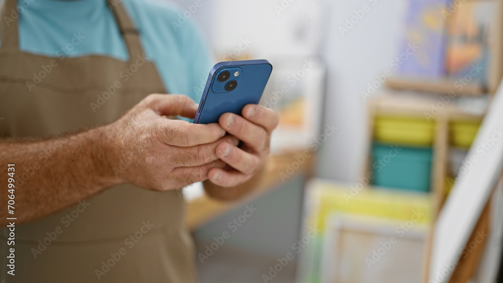 Handsome caucasian man artist acquires learning lessons online, typing a message on smartphone at captivating art studio inside college Handsome caucasian man artist acquires learning lessons online, typing a message on smartphone at captivating art studio inside college