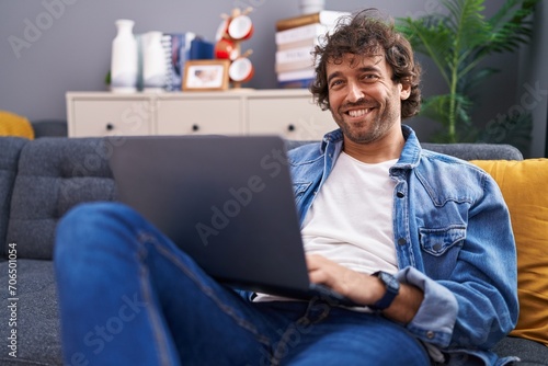 Young hispanic man using laptop sitting on sofa at home