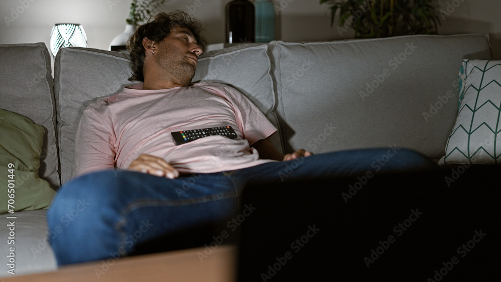Relaxed young man sleeping on a couch in a cozy living room, holding a remote