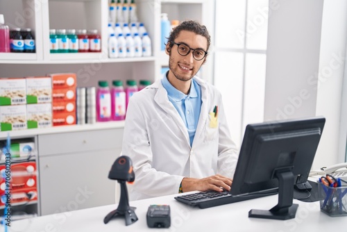 Young hispanic man pharmacist smiling confident using computer at pharmacy