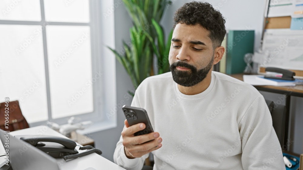 Focused hispanic man using smartphone in a modern office setting, portraying connectivity and work-life integration. Focused hispanic man using smartphone in a modern office setting, portraying connectivity and work-life integration.