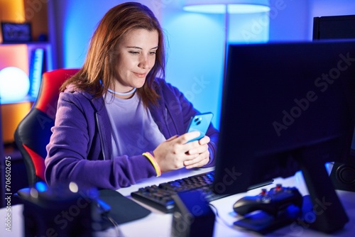 Young beautiful plus size woman streamer using computer and smartphone at gaming room