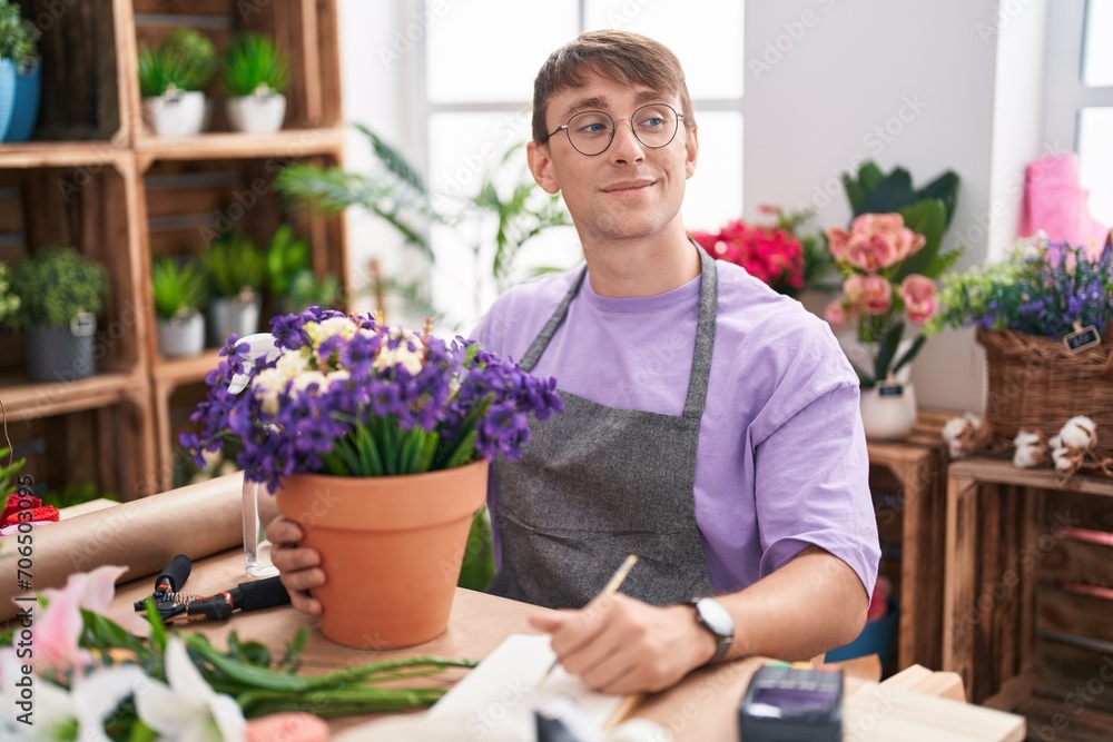 Caucasian blond man working at florist shop smiling looking to the side and staring away thinking.