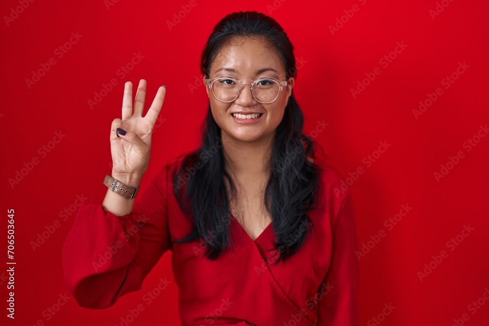Asian young woman standing over red background showing and pointing up with fingers number three while smiling confident and happy. Asian young woman standing over red background showing and pointing up with fingers number three while smiling confident and happy.