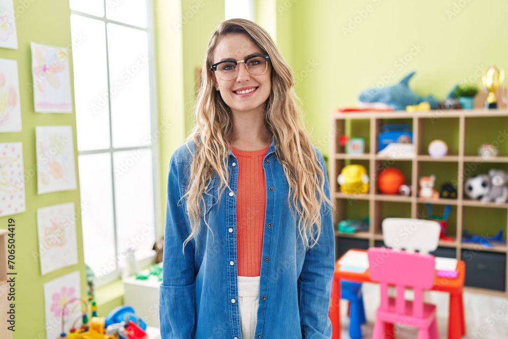 Young caucasian woman working as teacher at kindergarten looking positive and happy standing and smiling with a confident smile showing teeth Young caucasian woman working as teacher at kindergarten looking positive and happy standing and smiling with a confident smile showing teeth
