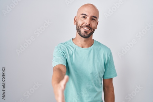 Middle age bald man standing over white background smiling friendly offering handshake as greeting and welcoming. successful business.