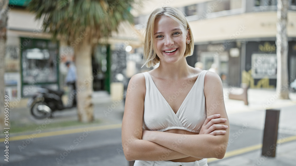 Young blonde woman standing with arms crossed gesture smiling at street