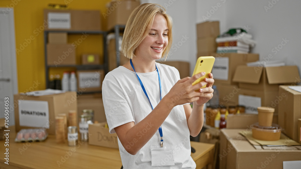 Young blonde woman volunteer using smartphone smiling at charity center Young blonde woman volunteer using smartphone smiling at charity center