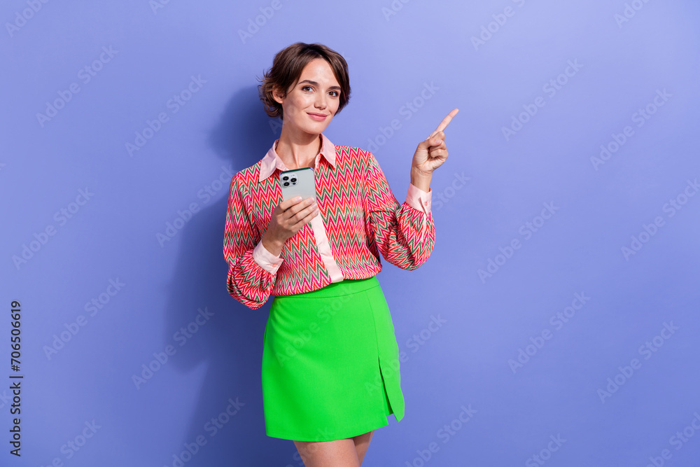 Photo portrait of pretty young girl point empty space hold device wear trendy print outfit isolated on violet color background Photo portrait of pretty young girl point empty space hold device wear trendy print outfit isolated on violet color background