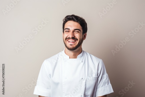 Portrait of a cheerful young chef in white uniform smiling against a neutral background. © Virtual Art Studio