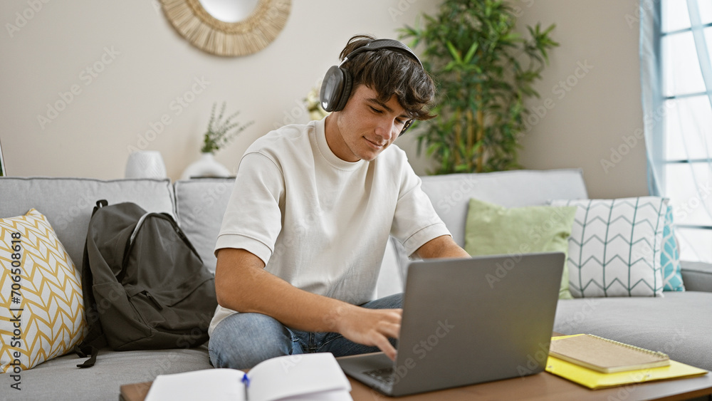 Obraz premium Confident young hispanic teenager relaxing, sitting on the sofa in his living room, immersed in studying online with his laptop, listening to his favorite music at home.