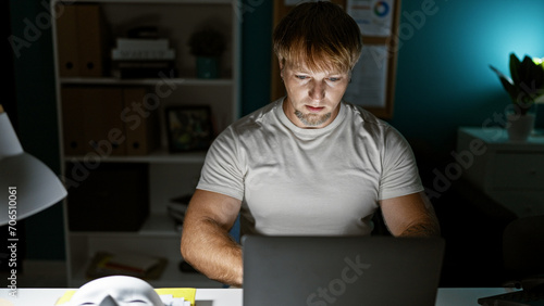 Bild auf Leinwand Focused young caucasian man working late on laptop in a home office setup, showcasing professionalism and dedication