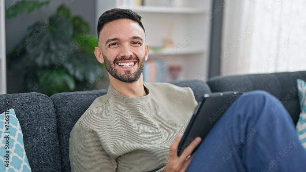 Young hispanic man using touchpad sitting on sofa at home Young hispanic man using touchpad sitting on sofa at home