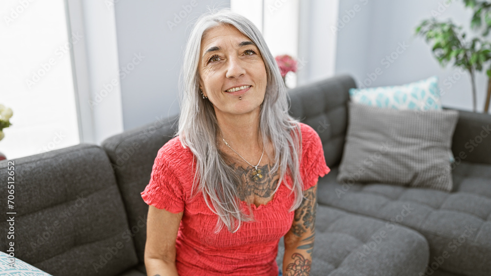 Confident middle age grey-haired woman enjoys a relaxing moment, cheerfully smiling while sitting comfortably on her cozy living room sofa at home Confident middle age grey-haired woman enjoys a relaxing moment, cheerfully smiling while sitting comfortably on her cozy living room sofa at home