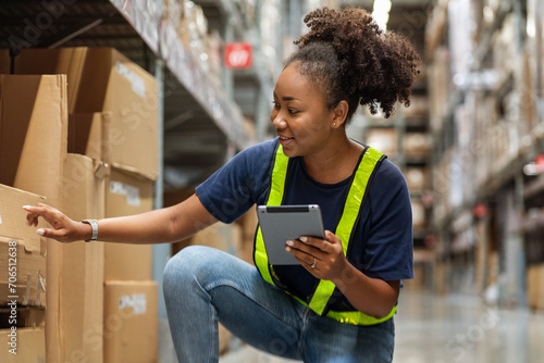 Young black African American woman holding a tablet sits checking inventory and checking orders from customers, picking up boxes from shelves to deliver documents to customers in warehouse wholesale  © Supavadee
