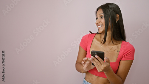 Young latin woman using smartphone looking to the side surprised over isolated pink background
