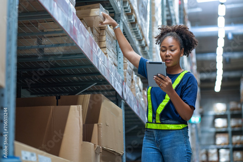 Black African American woman holding a tablet sits checking inventory and checking orders from customers, picking up boxes from shelves to deliver documents to customers in warehouse wholesale store. photo