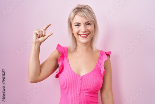 Young caucasian woman standing over pink background smiling and confident gesturing with hand doing small size sign with fingers looking and the camera. measure concept. © Krakenimages.com