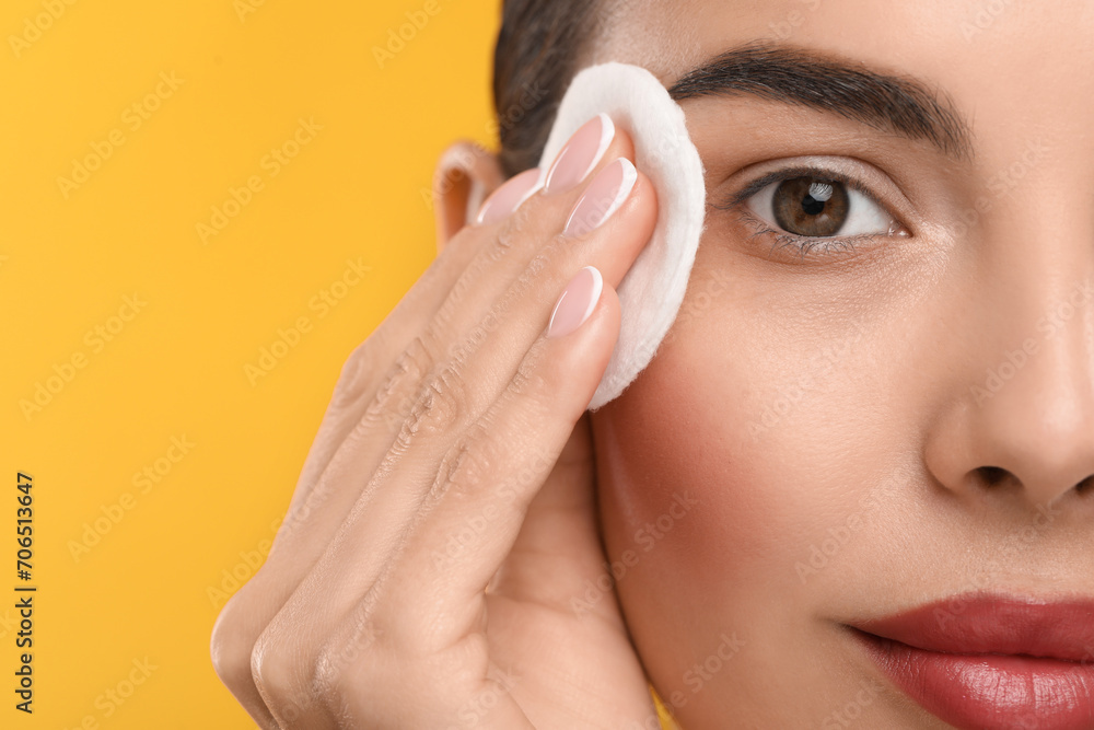 Beautiful woman removing makeup with cotton pad on orange background, closeup. Space for text