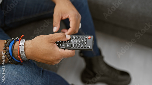 African american man in casual attire holding a remote control at home, symbolizing leisure and technology use.