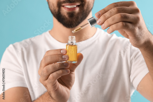 Man with cosmetic serum in hands on light blue background, closeup