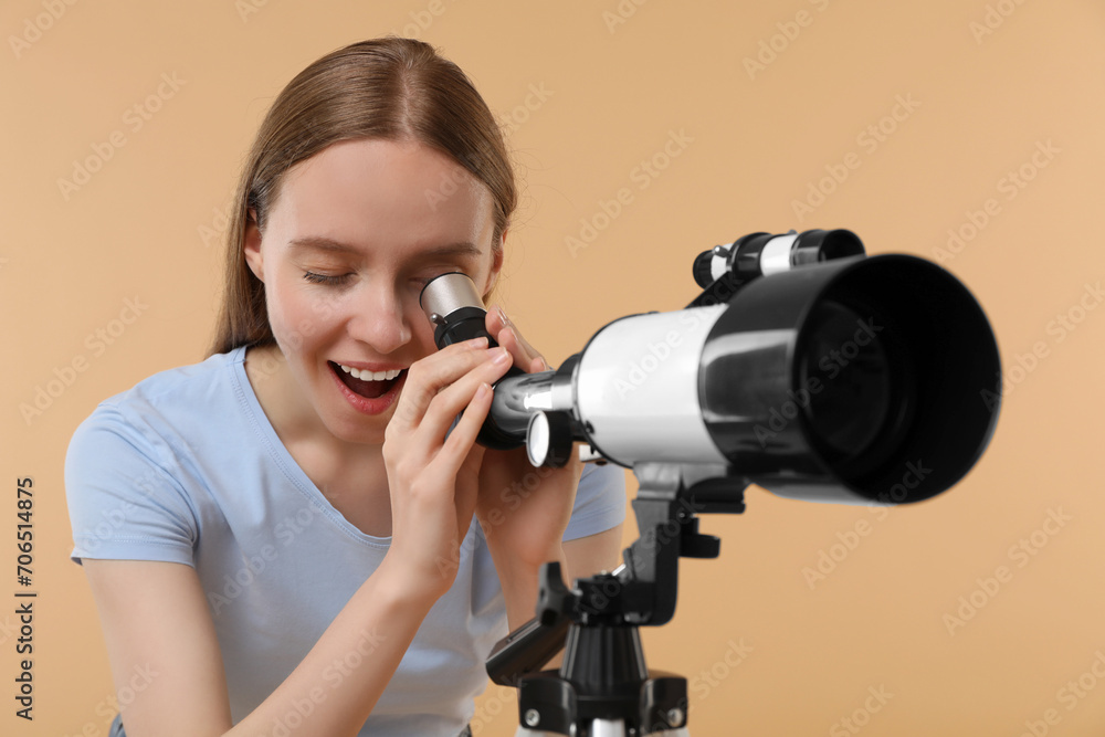 Young astronomer looking at stars through telescope on beige background Young astronomer looking at stars through telescope on beige background