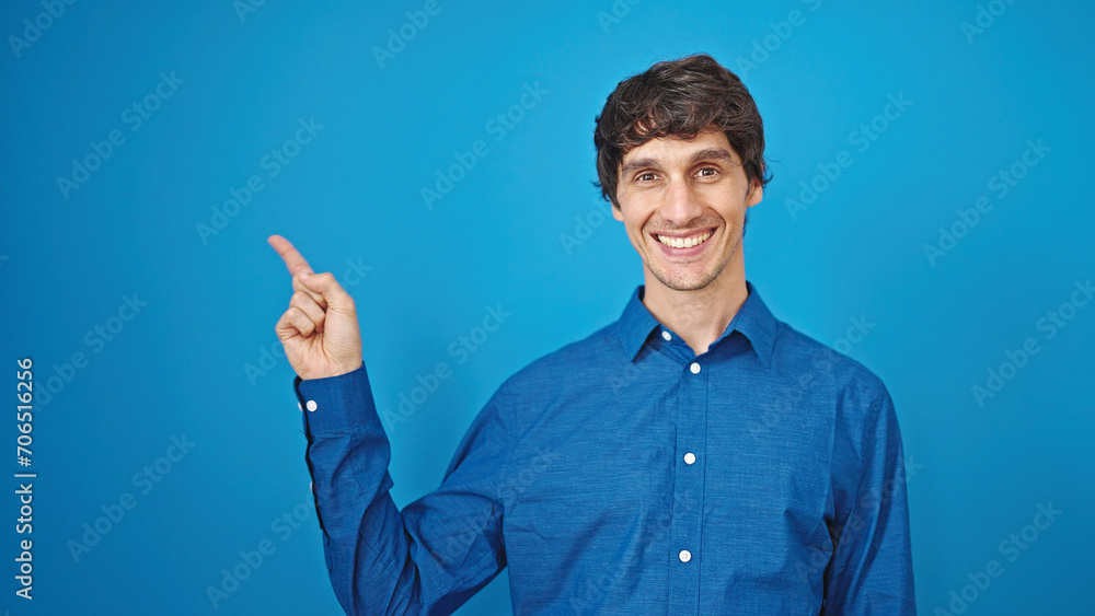 Young hispanic man smiling pointing to the side over isolated blue background Young hispanic man smiling pointing to the side over isolated blue background