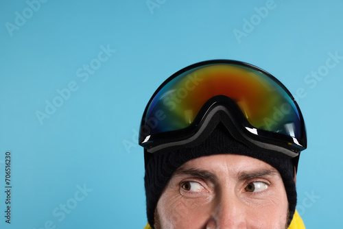 Winter sports. Man in ski goggles on light blue background, closeup with space for text