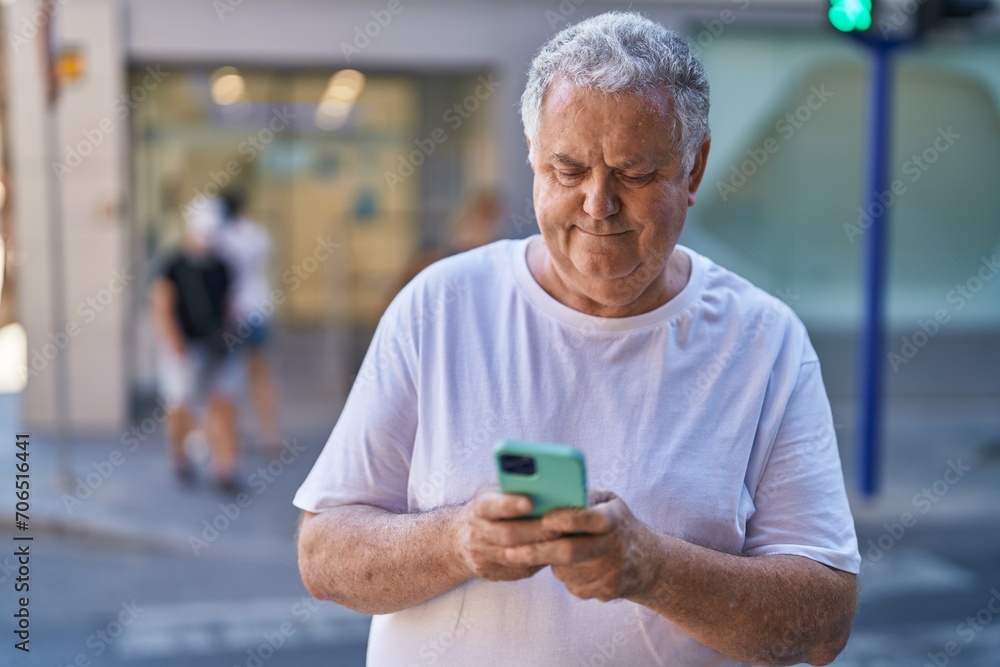 Middle age grey-haired man using smartphone with relaxed expression at street Middle age grey-haired man using smartphone with relaxed expression at street